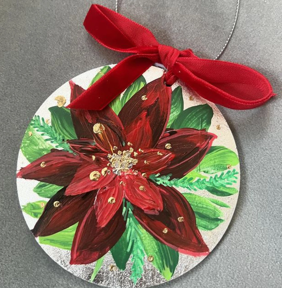 Round ornament featuring a hand-painted red poinsettia with green leaves, accented by a red ribbon tied in a bow at the top.