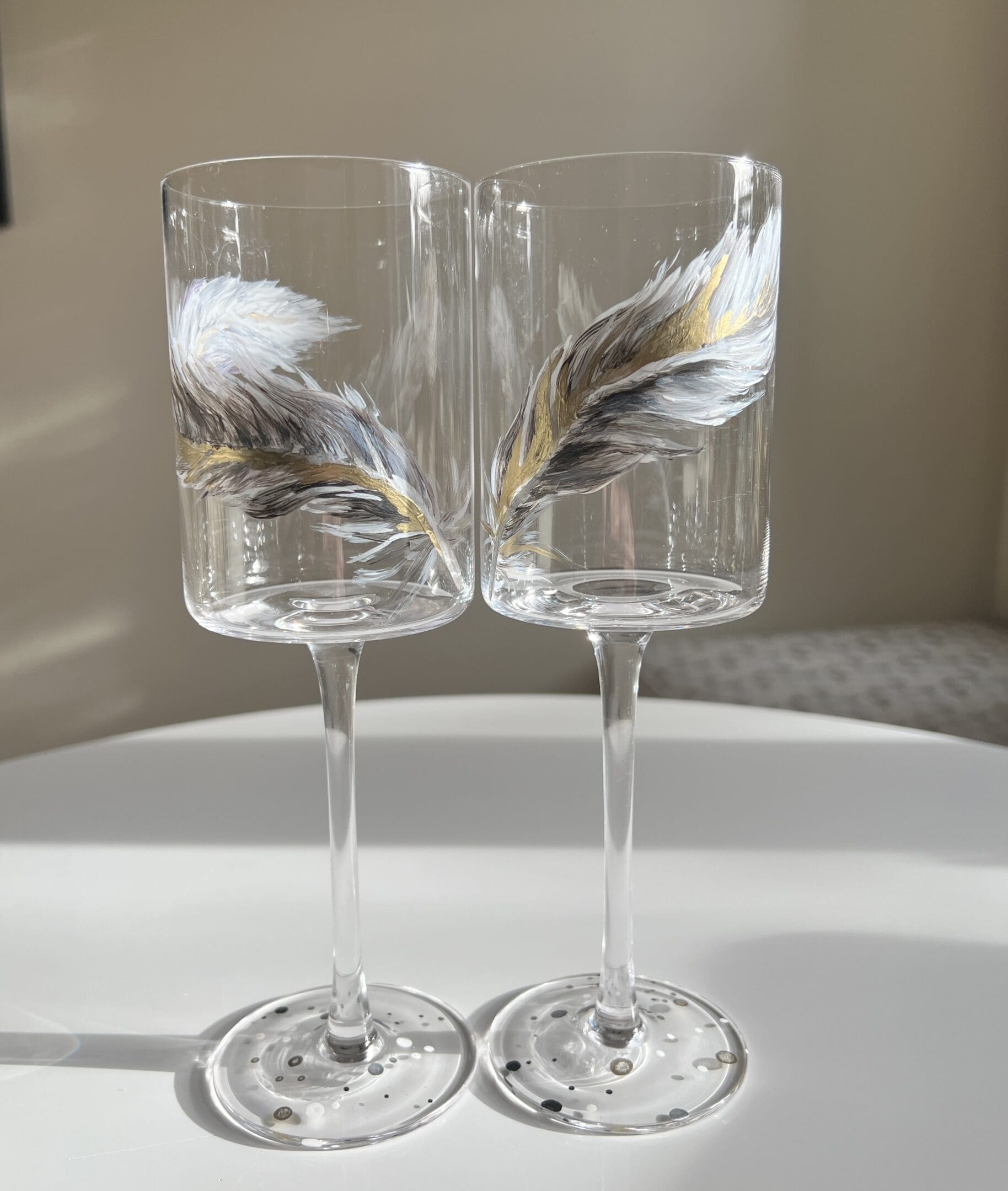 Two wine glasses with feathers on them sitting on a table.