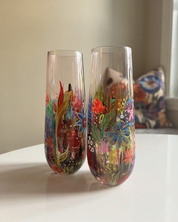 Two glasses with flowers painted on them sitting on a table.